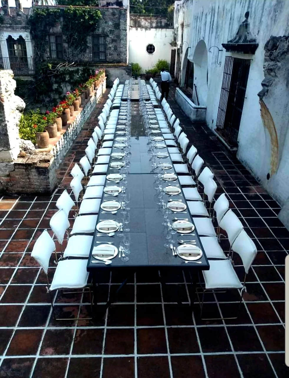 Mesa larga negra con sillas blancas en patio histórico
